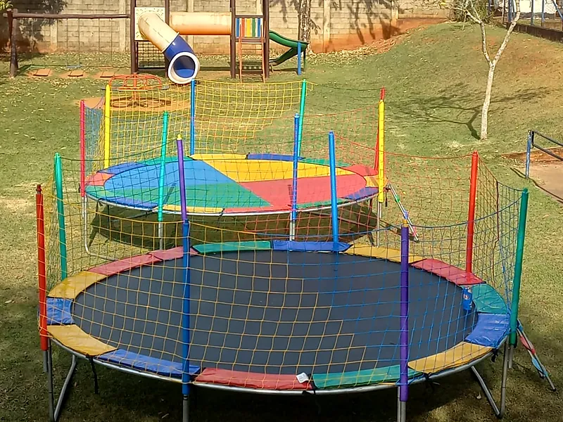 Duas camas elásticas coloridas com rede de proteção em um gramado
