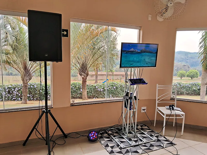Karaokê montado com TV em pedestal, controle touch e caixa de som profissional